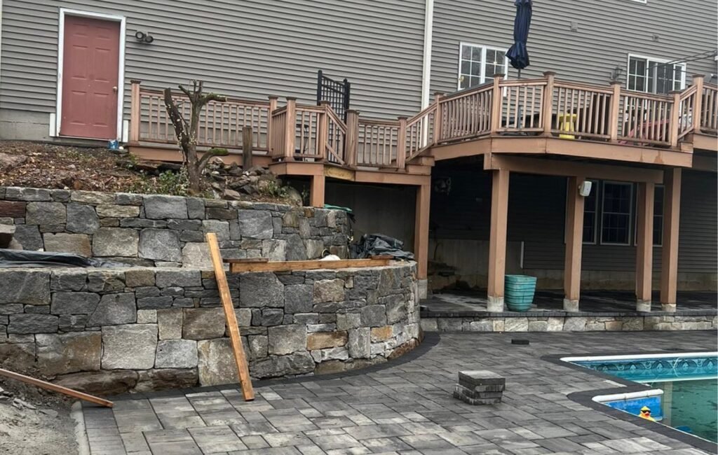 Curved stone retaining wall and paver patio being built beside a backyard pool