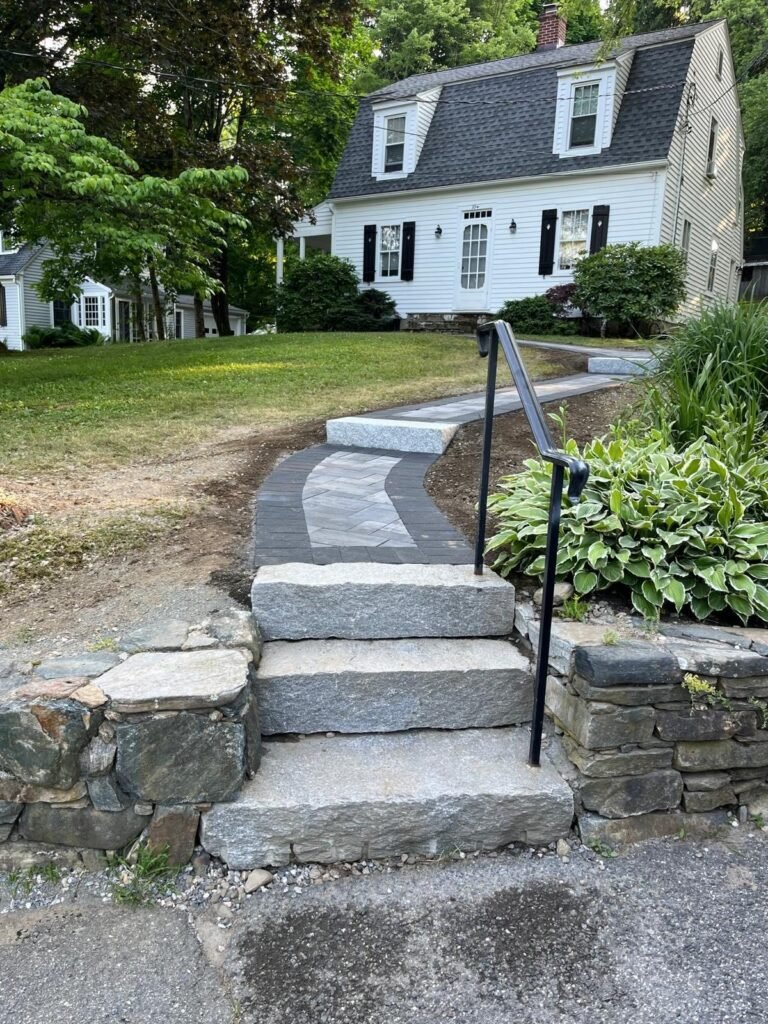 New stone steps with a metal handrail leading to a paver walkway and stone retaining walls